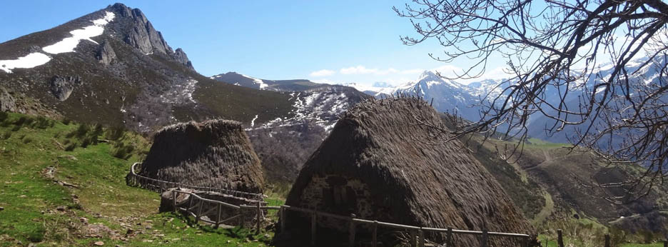 Dos teitos de Teverga en primer plano con montañas al fondo. Brañas de Teverga